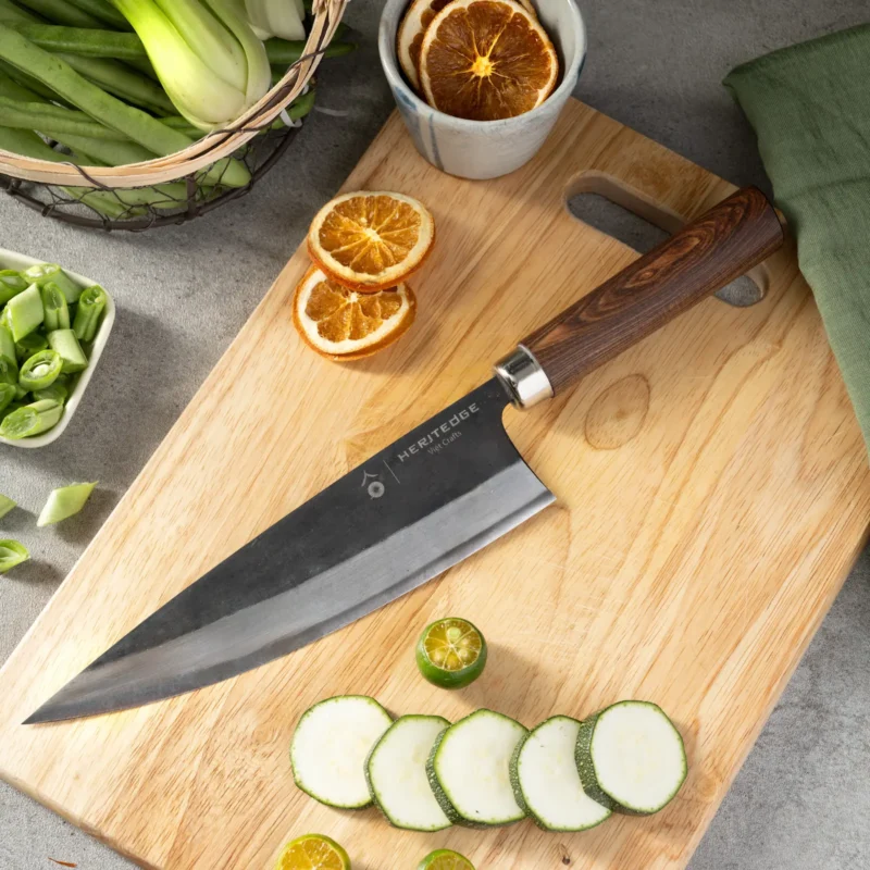 Heritedge Küchenmesser Long Classic mit Carbonstahlklinge auf Holzbrett, umgeben von getrockneten Orangen und frischem Gemüse